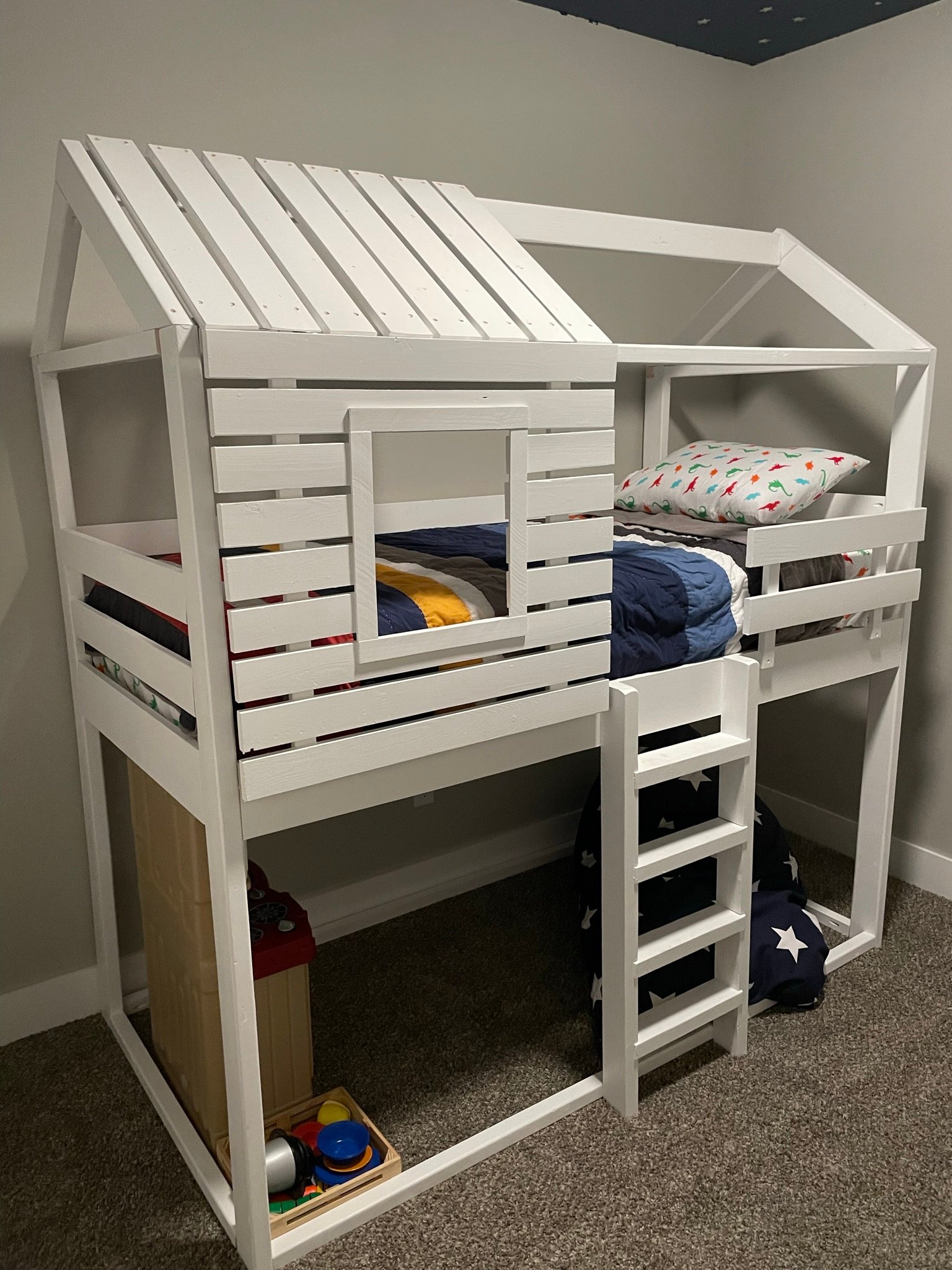 White wooden house-shaped bed frame with a dinosaur pillow by Westerman Woodworks, Tulsa, Oklahoma